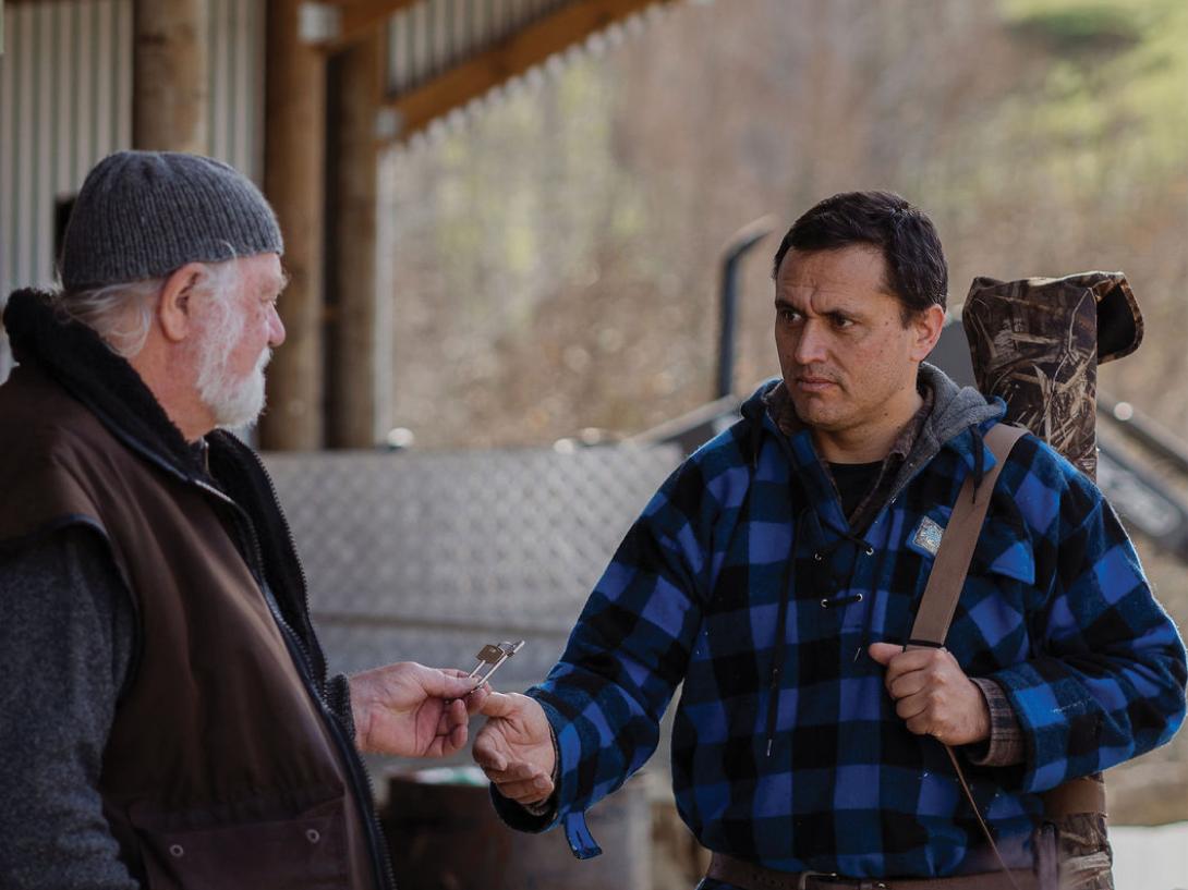 Older white man giving keys to a younger maori man wearing hunting gear